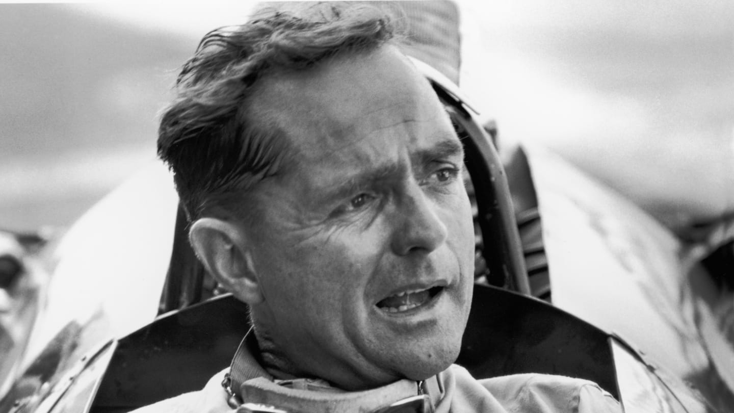 American Grand Prix racing car driver Phil Hill sits in his car and talks to the out-of-frame pit